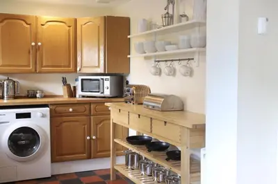 a kitchen with wooden cabinets and a washer and dryer at Abbey Cottages- Heron House in Talley