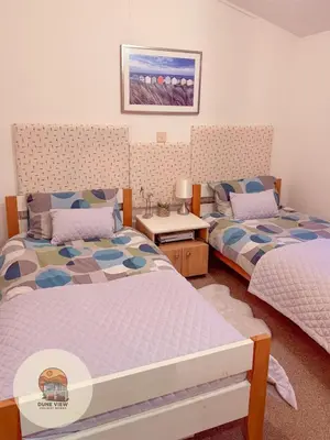 a bedroom with two beds and a table with a lamp at Dune View Chalet in Ynys-lâs Station