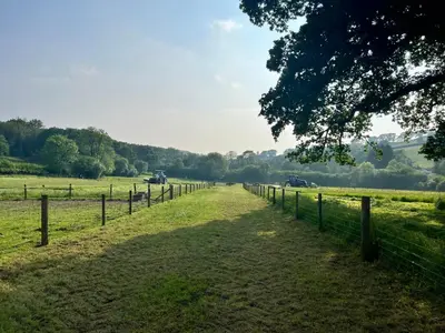 a fence next to a field with cars on a road at Oakies Farm Stays XL in Llandovery