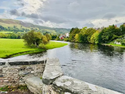 a river with a stone wall next to a field at Henllys Cottage in Corwen