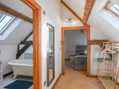 a bathroom with a bath tub and a bedroom at The Byre At Woodgate Farm in Church Stretton