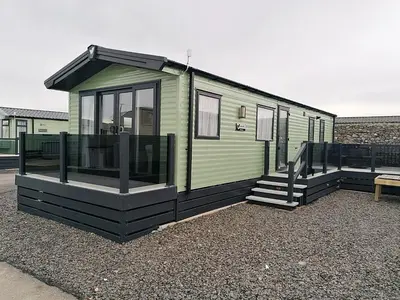 a green tiny house sitting on top of gravel at Seaview Caravan f17 at Neptune Park, Tywyn in Tywyn
