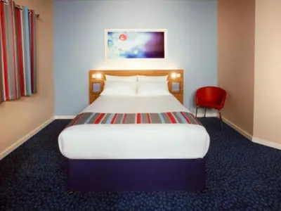 a bedroom with a large bed and a red chair at Travelodge Shrewsbury Bayston Hill in Meole Brace
