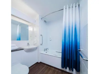 a white bathroom with a blue shower curtain and a sink at Travelodge Shrewsbury Bayston Hill in Meole Brace