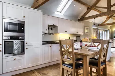 a kitchen with white cabinets and a wooden table and chairs at Long Barn in Ludlow