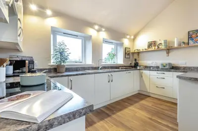 a kitchen with white cabinets and wooden floors and windows at 3 Bed in Lyonshall oc-h34806 in Lyonshall