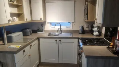 a kitchen with white cabinets and a sink and a stove at Privately owned Pet friendly caravan in Llanddwywe