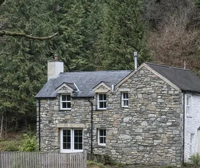 a stone house in front of a forest at Ferndale Cottage in Church Stretton