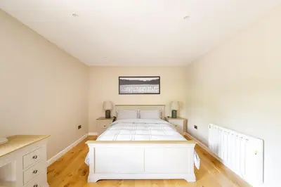 a white bedroom with a white bed and wooden floors at Luxury Lakeside Lodge with Hot Tub in Ratlinghope in Ratlinghope