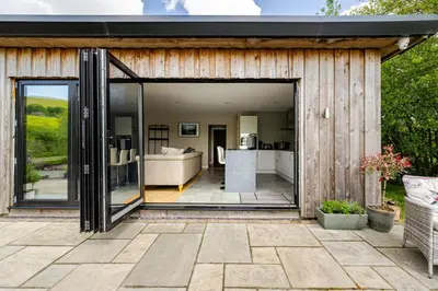 a wooden house with a large sliding glass door at Luxury Lakeside Lodge with Hot Tub in Ratlinghope in Ratlinghope
