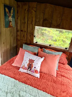 a bed with red sheets and pillows with a window at Nesta's Nook in Llandovery