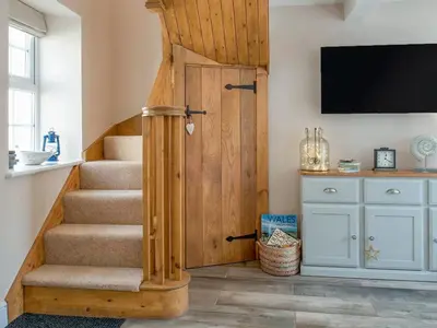 a staircase with a wooden door and a television on a wall at Seagrass Cottage in Aberdyfi