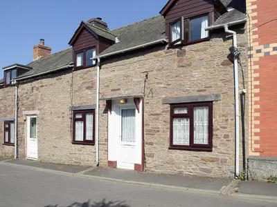 an old brick building with a white door and windows at Canon's Cottage in Clun