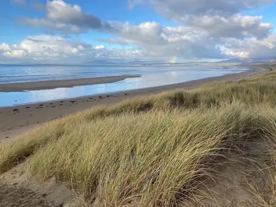 a sandy beach with grass and the ocean at Harlech castle and beach home in Harlech