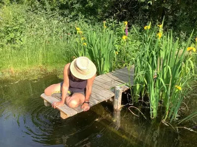 a person in a hat sitting on a dock in the water at Off Grid living high in the hills in Picklescott