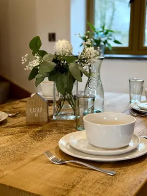 a table with a plate and a bowl and vases with flowers at Y Beudy Bach in Llanfor