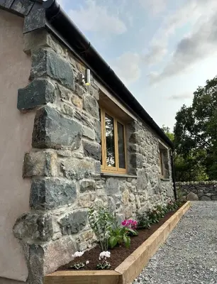 a stone house with a window and flowers at Y Beudy Bach in Llanfor