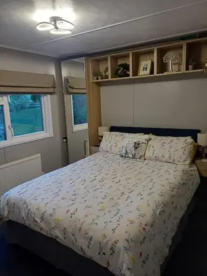 a bedroom with a bed with a comforter and two windows at The Little lodge on the lake in Welshpool