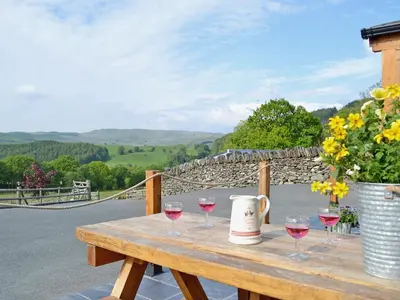 a wooden table with wine glasses and a bucket of flowers at Golygfar Mynydd - Mountain View in Strata Florida