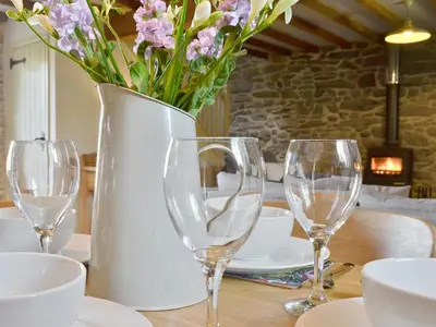 a vase with flowers in it on a table with glasses at Ivy Bush Cottage in Llanddewi-Brefi