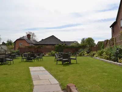 a patio with tables and chairs on a lawn at Red Lion Lodge in Myddle