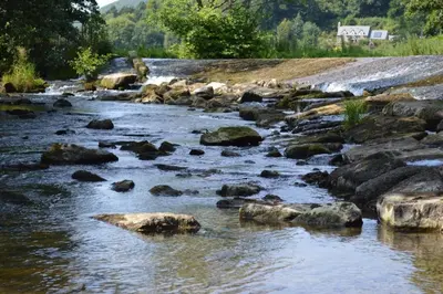 a river with rocks and a house in the background at Riverside Inn, Aymestrey in Aymestrey