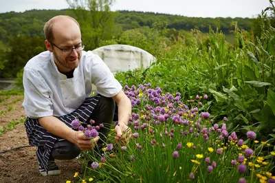 a man kneeling down in a garden smelling purple flowers at Riverside Inn, Aymestrey in Aymestrey