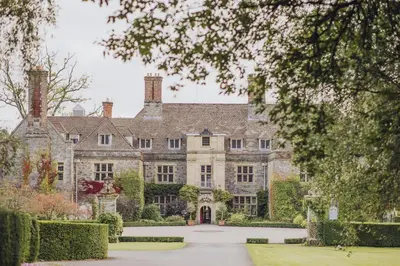an old stone house with a driveway and trees at Llangoed Hall in Bronllys