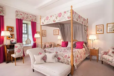 a bedroom with a canopy bed and a chair at Llangoed Hall in Bronllys