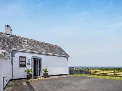a white building with a garage with the ocean in the background at Bay View Cottage in Llanon