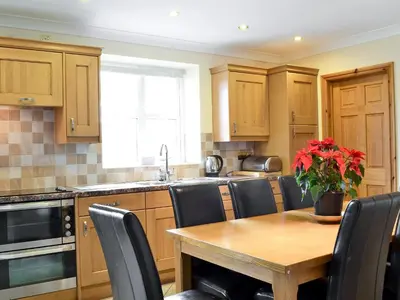 a kitchen with wooden cabinets and a wooden table with chairs at 4 Pengraig Draw in Llanychaiarn