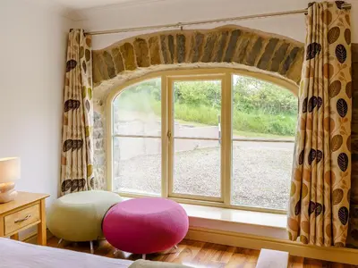 a bedroom with a large window and a pink stool at Cwmhyfryd in Llanllwchaiarn