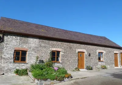 a brick building with brown doors and flowers at Beudy Bach in Lampeter