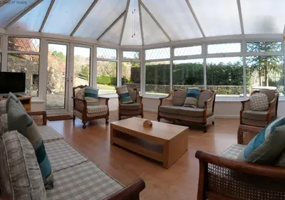 a living room with chairs and a table in a conservatory at Ysgubor Illtyd in Dolgellau