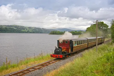 a train traveling down the tracks next to a body of water at Troed yr Aran in Aber Cowarch