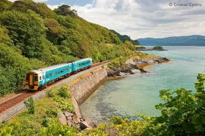 a train traveling down the tracks next to a river at Ysgubor y Waun in Tywyn