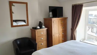 a bedroom with a dresser with a television and a chair at Byrdir House in Harlech