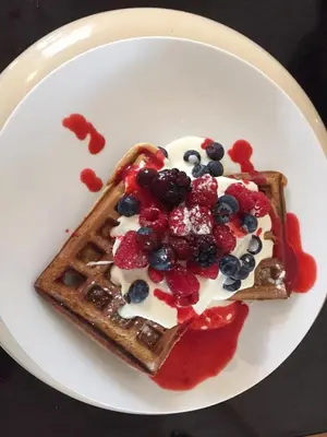 a white plate with waffles with berries and cream at The Town House BnB in Brecon