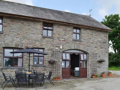 a stone house with a table and an umbrella at Ty Coch Cottage in Dihewid