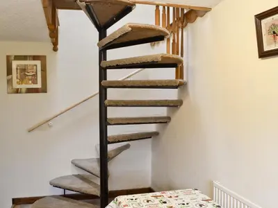 a spiral staircase in a house with a bed at Ty Coch Cottage in Dihewid