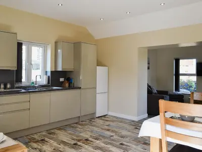 a kitchen with white cabinets and a living room at Roath in Cilcennin