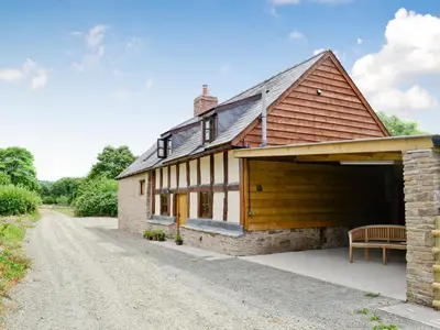 a barn conversion with a garage and a bench on a dirt road at Mill Cottage in Peterchurch