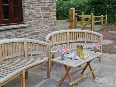 two wooden benches sitting next to a table with flowers at Mill Cottage in Peterchurch