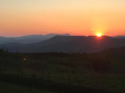 a sunset over the mountains with the sun setting on the horizon at Foel Fach in Talerddig