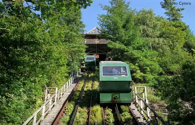 a green train on the tracks with a building at Foel Fach in Talerddig