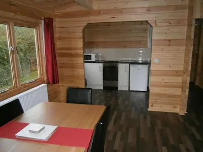 a dining room with a table and a kitchen at Long Mountain Centre Log Cabins in Meadowtown