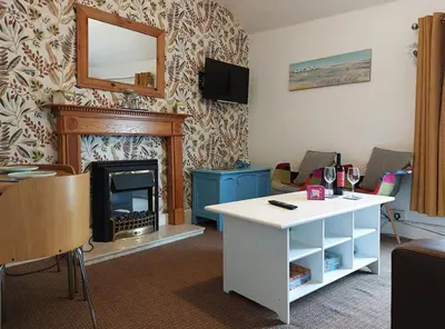 a living room with a fireplace and a white table at Salt Marsh Apartment in Tywyn