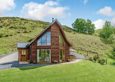 a small wooden house with a hill behind it at Slate House Lodges in Towyn