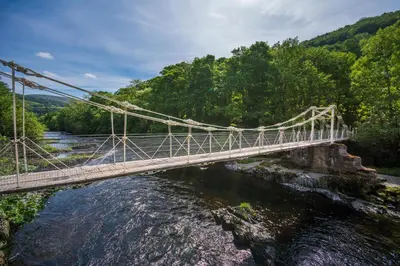 a suspension bridge over a river with trees at The Chainbridge Hotel in Llangollen