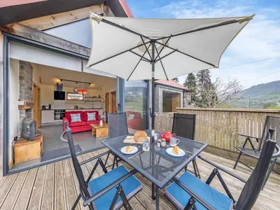a table and chairs on a deck with an umbrella at Wern Ddu Cottage in Pen-y-bont-fawr